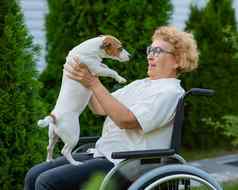 上了年纪的高加索人女人拥抱杰克罗素梗狗坐着轮椅走在户外