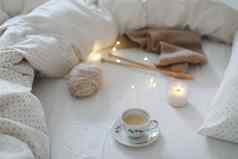 舒适的早....生活咖啡杯蜡烛针羊毛纱白色床上针织温暖的羊毛毛衣围巾前视图舒适生活方式舒适的情绪工艺品一天概念