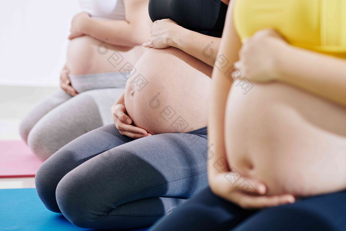 集团普雷甘特年轻的女性参加瑜伽类触碰肚子坐着瑜伽垫