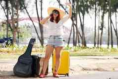 快乐的年轻的女人站在户外手提箱吉他会说话的电话捕捉出租车