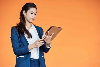 年轻的女企业家阅<strong>读文章</strong>平板电脑电脑孤立的橙色