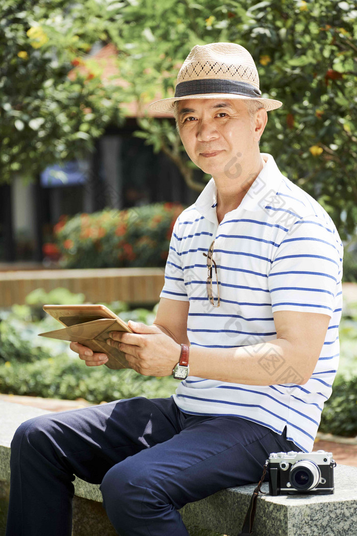 成熟的中国人男人。稻草他坐着在户外数字相机阅读文章平板电脑电脑