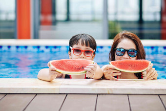 妈妈。女儿太阳镜站游泳池吃甜蜜的美味的西瓜片