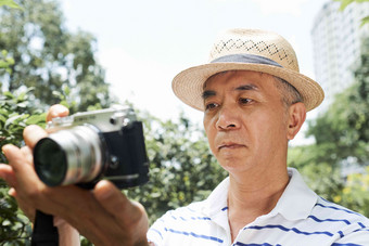 高级亚洲男人。屏幕数字相机检查照片当地的公园