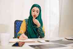 年轻的美丽的穆斯林女商人传统的衣服会说话的电话的同事采取笔记规划师杂志