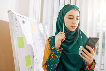 肖像年轻的穆斯林女商人传统的衣服阅<strong>读文章</strong>智能手机屏幕