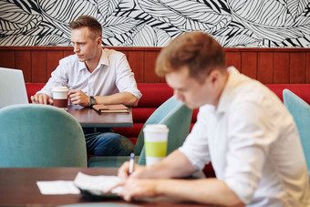 年轻的自由职业者杯咖啡坐着咖啡馆表格阅读文章移动PC屏幕