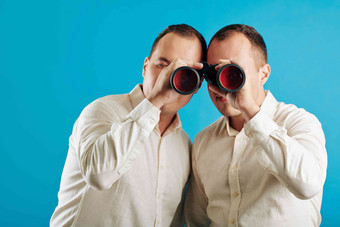 认不出来双胞胎兄弟穿白色衬衫双筒望远镜相机蓝色的墙背景