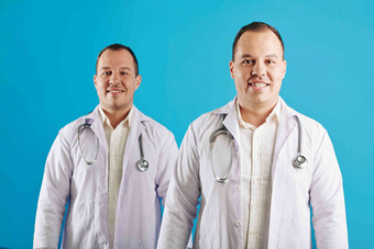 水平工作室肖像双胞胎兄弟穿白色外套工作医生站蓝色的墙背景微笑