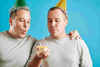 水平工作室肖像年轻的成人双胞胎兄弟站小一块生日蛋糕吹蜡烛