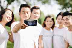 年轻的微笑志愿者photograhing朋友智能手机有选择性的焦点