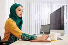 穆斯林年轻的女人采取笔记规划师工作编程代码项目