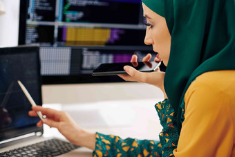 穆斯林女开发人员检查编程代码移动PC屏幕记录的声音消息同事客户端