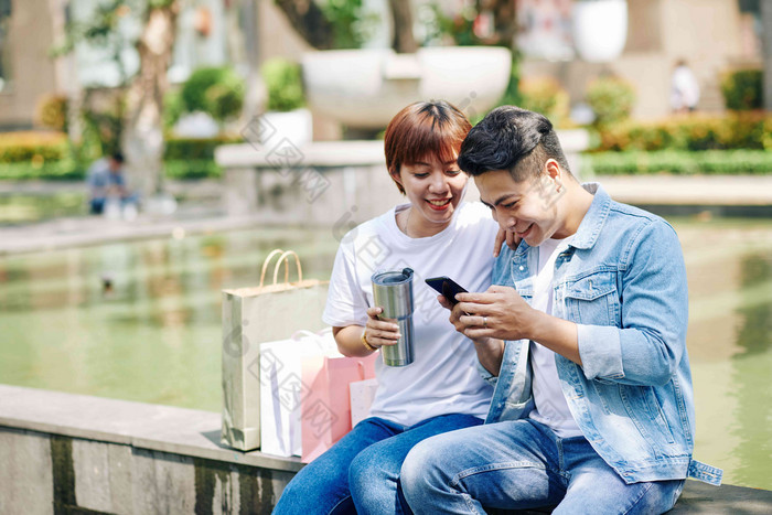 快乐年轻的亚洲夫妇休息喷泉喝咖啡热水瓶检查社会媒体智能手机