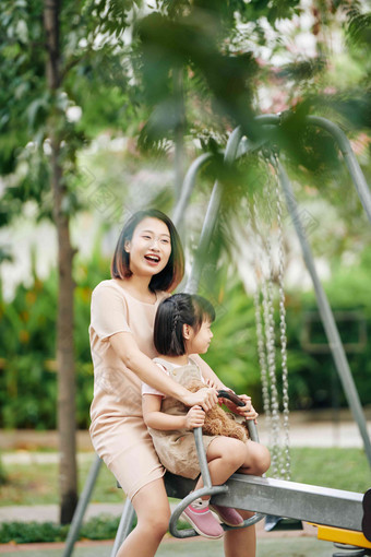 快乐的年轻的越南女人坐着<strong>跷跷板</strong>女儿支出时间操场上