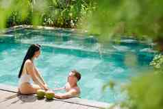 快乐年轻的夫妇爱支出时间游泳池度假胜地持有手