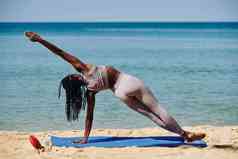 适合黑色的年轻的女人扩展一边板材瑜伽席海滩