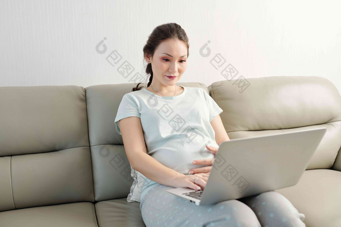 可爱的年轻的亚洲怀孕了女人休息沙发阅读文章移动PC屏幕