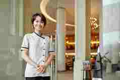 肖像快乐的年轻的亚洲酒店经理站入口门微笑相机