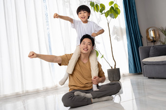 房间里一位亚洲男孩骑在父亲的肩膀上玩耍家