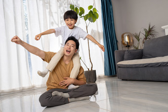 房间里一位亚洲男孩骑在父亲的肩膀上玩耍