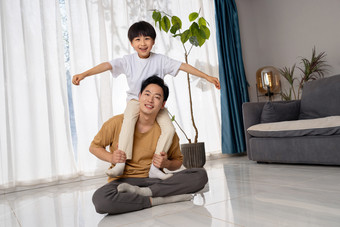 房间里一位亚洲男孩骑在父亲的肩膀上玩耍客厅
