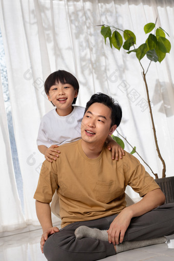 房间里一位亚洲男孩趴在父亲的肩膀上玩耍儿子