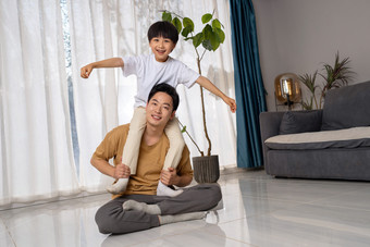 房间里一位亚洲男孩骑在父亲的肩膀上玩耍中国
