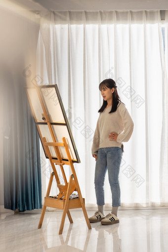 房间里一位亚洲华裔青年女人站在画架前住宅房间素材