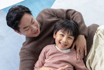 俯瞰房间里一位亚洲男孩和父亲躺在地板上玩耍嬉戏的
