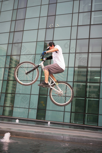 男青年在写字楼下玩自行车跳跃