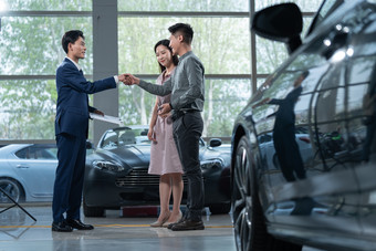 汽车销售人员和青年夫妇<strong>握手</strong>站着素材