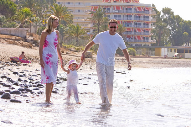 年轻健康的家庭在阳光明媚的海滩上散步