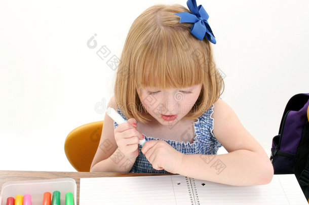 漂亮的小女孩坐在桌子旁，拿着一盒马克笔和笔记本