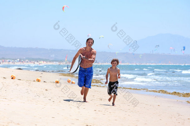 年轻的父子带着冲浪板在沙滩上奔跑