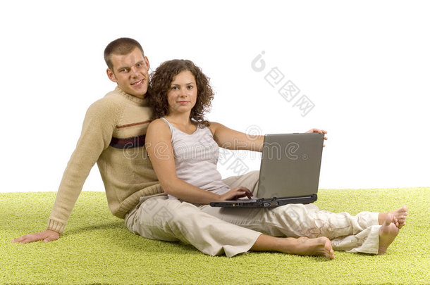 一对年轻夫妇带着笔记本电脑在绿地毯上