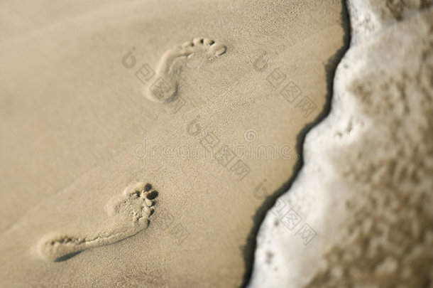在波浪旁边的沙滩上留下脚印。