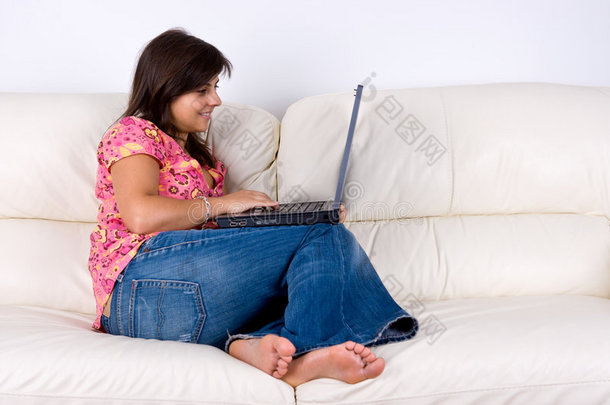 坐在<strong>白色沙发</strong>上的拿着笔记本电脑的年轻女子