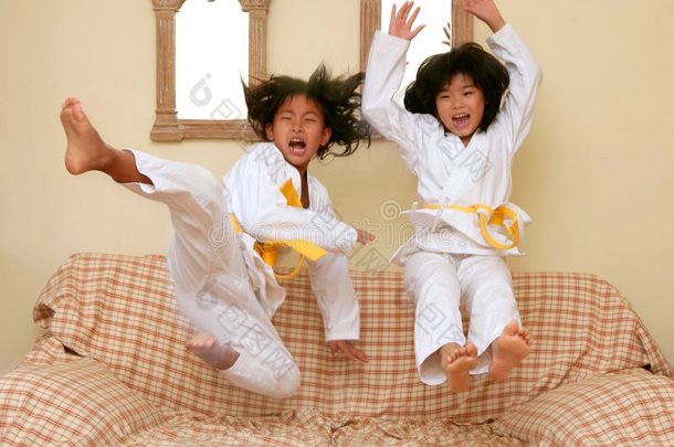 两个亚洲柔道小女孩在沙发上跳
