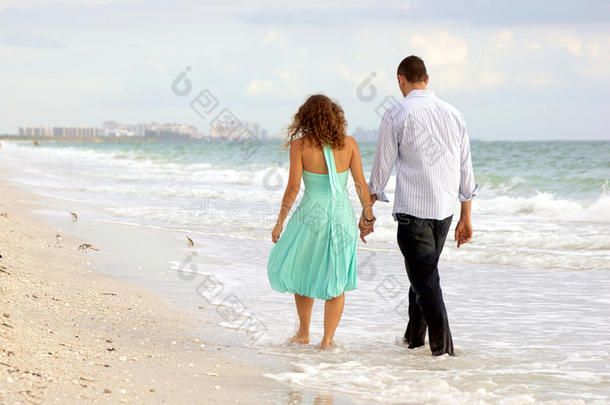 一对年轻夫妇<strong>手牵手</strong>在海滩上<strong>散步</strong>