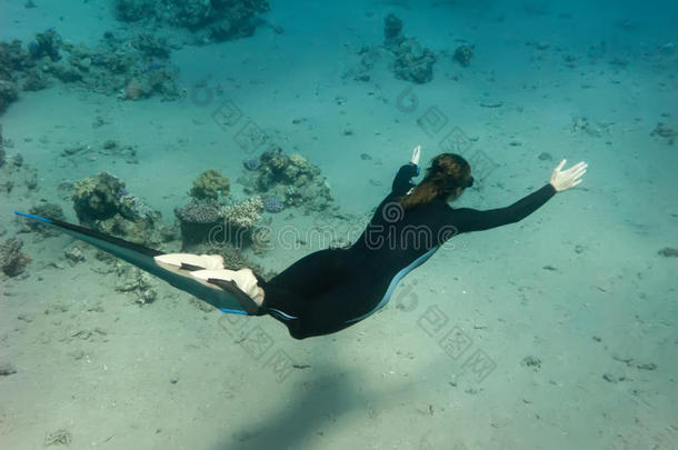 自由潜水员女孩沿着沙海底游泳