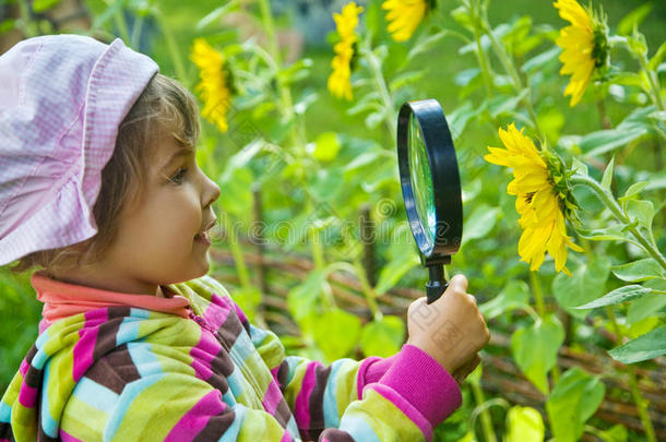 小女孩拿着放大镜看着花