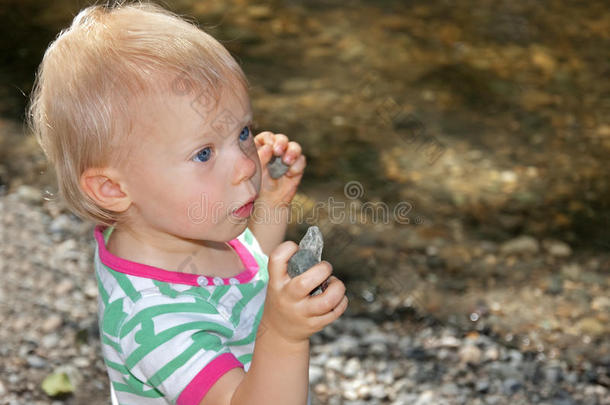 可爱的蹒跚学步的孩子在海滩上拿着石头