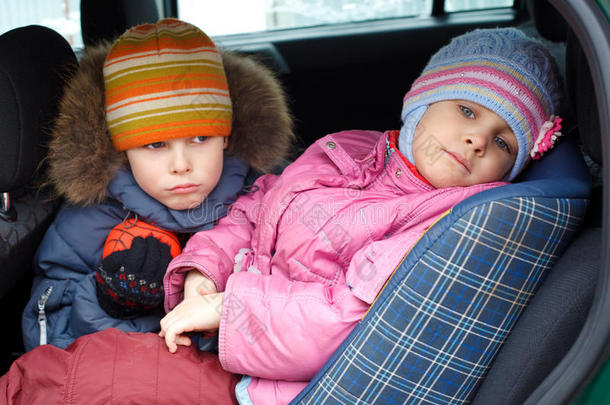 伤心的男孩和女孩，穿着冬天的衣服在车里。