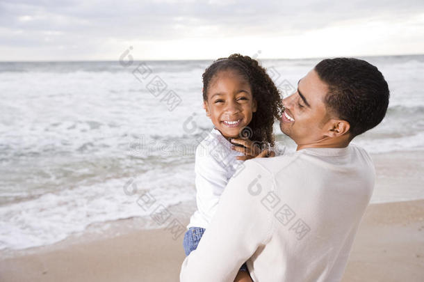 非洲裔美国人爸爸在海滩抱着小女孩