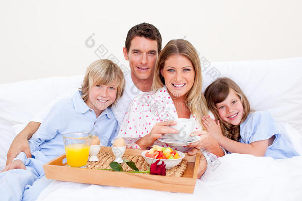 微笑的一家人坐在床上吃早餐