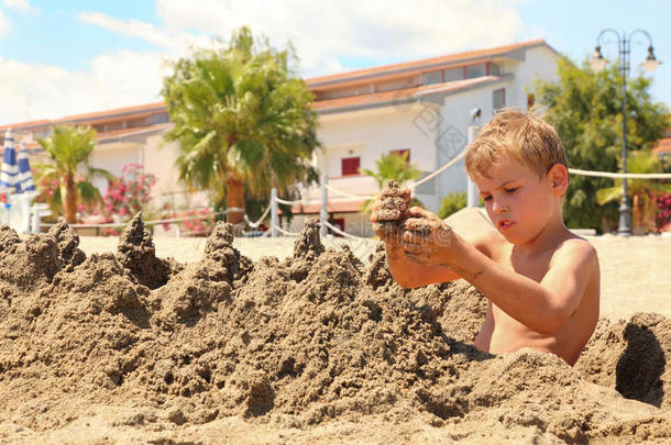海滩上的男孩坐在那里，用沙子模拟山丘