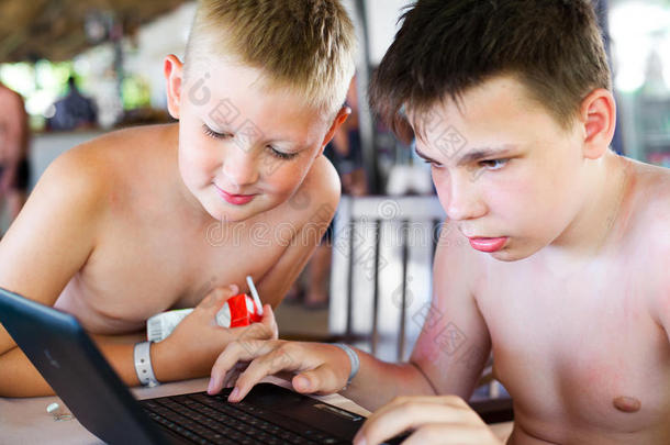 两个男孩在海滩上的酒吧里休息时玩笔记本电脑