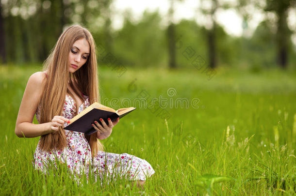 女学生坐在草地上读<strong>课本</strong>。