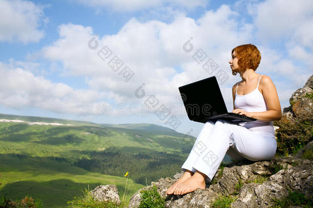 坐在悬崖边上拿着笔记本电脑的女人